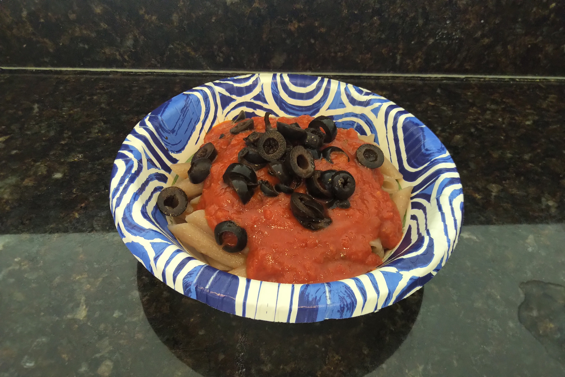 Bowl of gluten free cassave penne pasta topped with marinara sauce and olives
