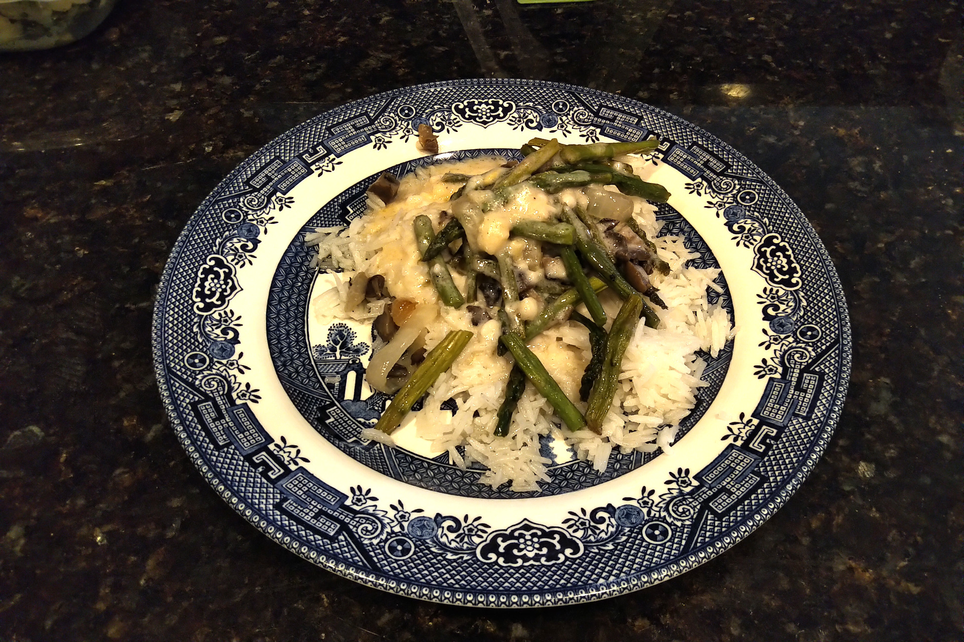Plate of asparagus, onions, and mushrooms with cheese sauce over rice